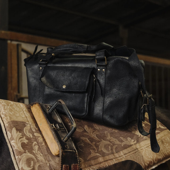 Black jabari boar leather bag on a textured surface with a dark background inside of a barn