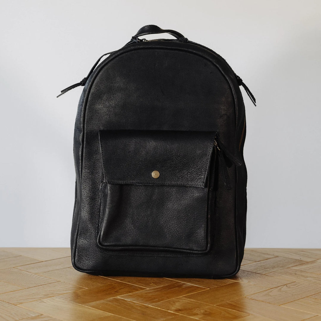 Black leather backpack on a wooden floor with a white wall background