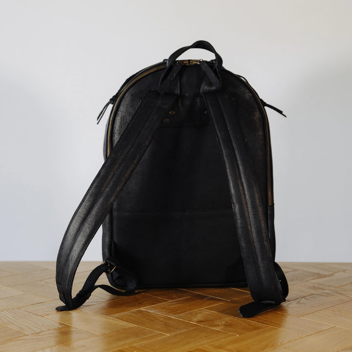 Black jabari boar leather backpack on a wooden floor with a white wall background