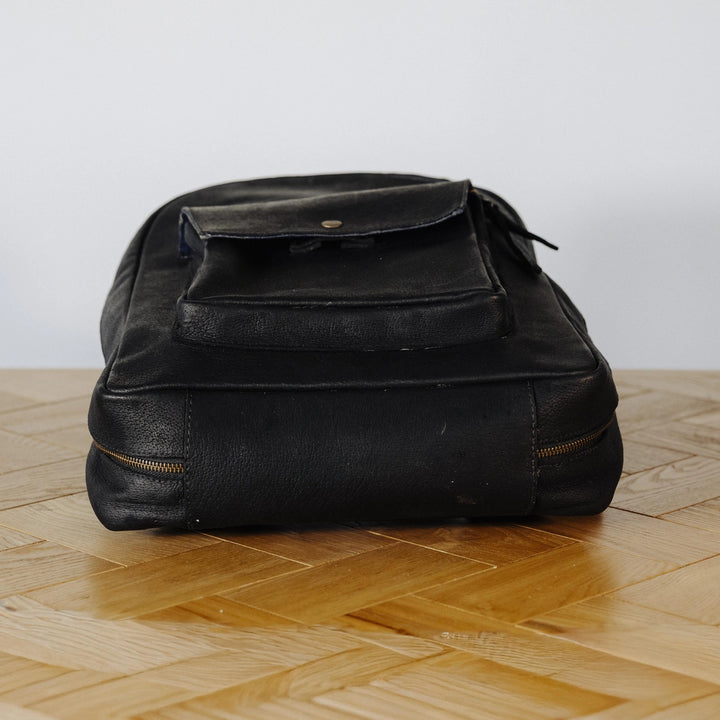 Black leather backpack on a wooden floor with a white wall background