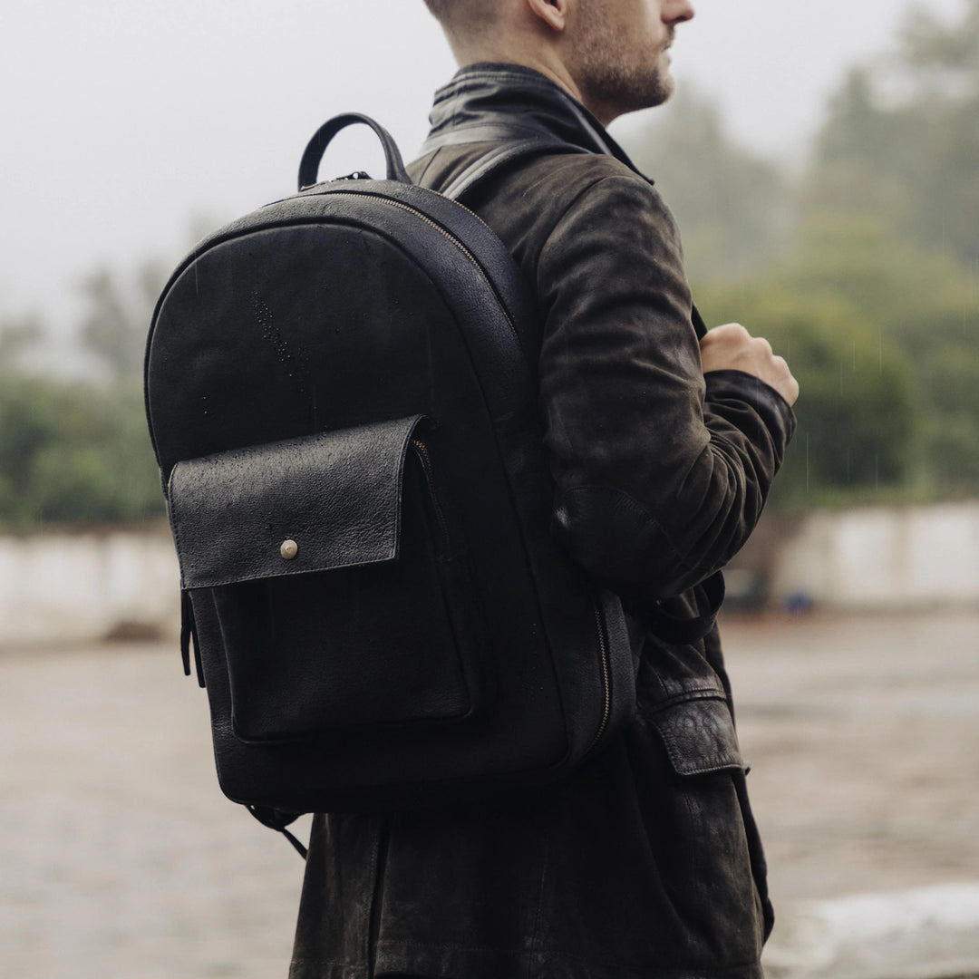 Man wearing a black jabari boar leather backpack with dark brown suede leather jacket outdoors with a blurred background