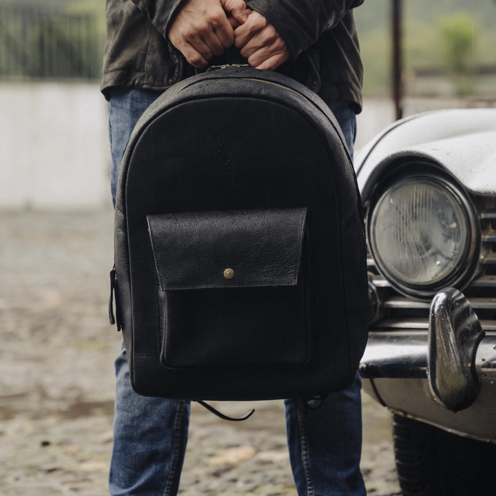 Man holding a black jabari boar backpack with a vintage car in the background
