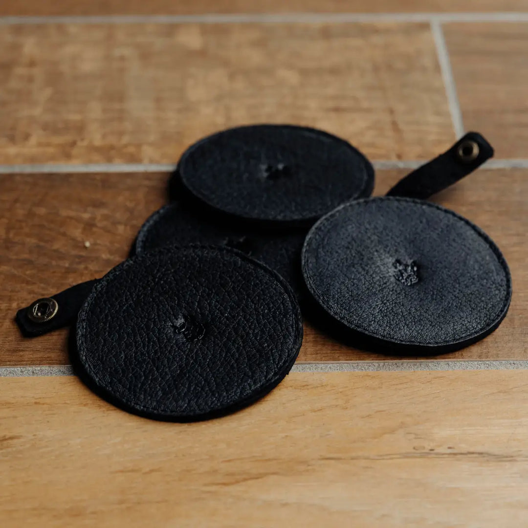 Four black leather coasters on a wooden surface