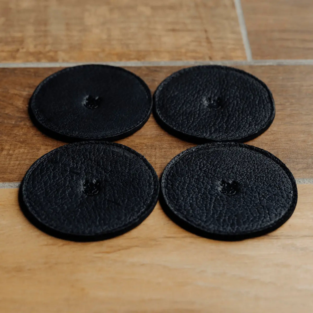 Four black round coasters on a wooden surface