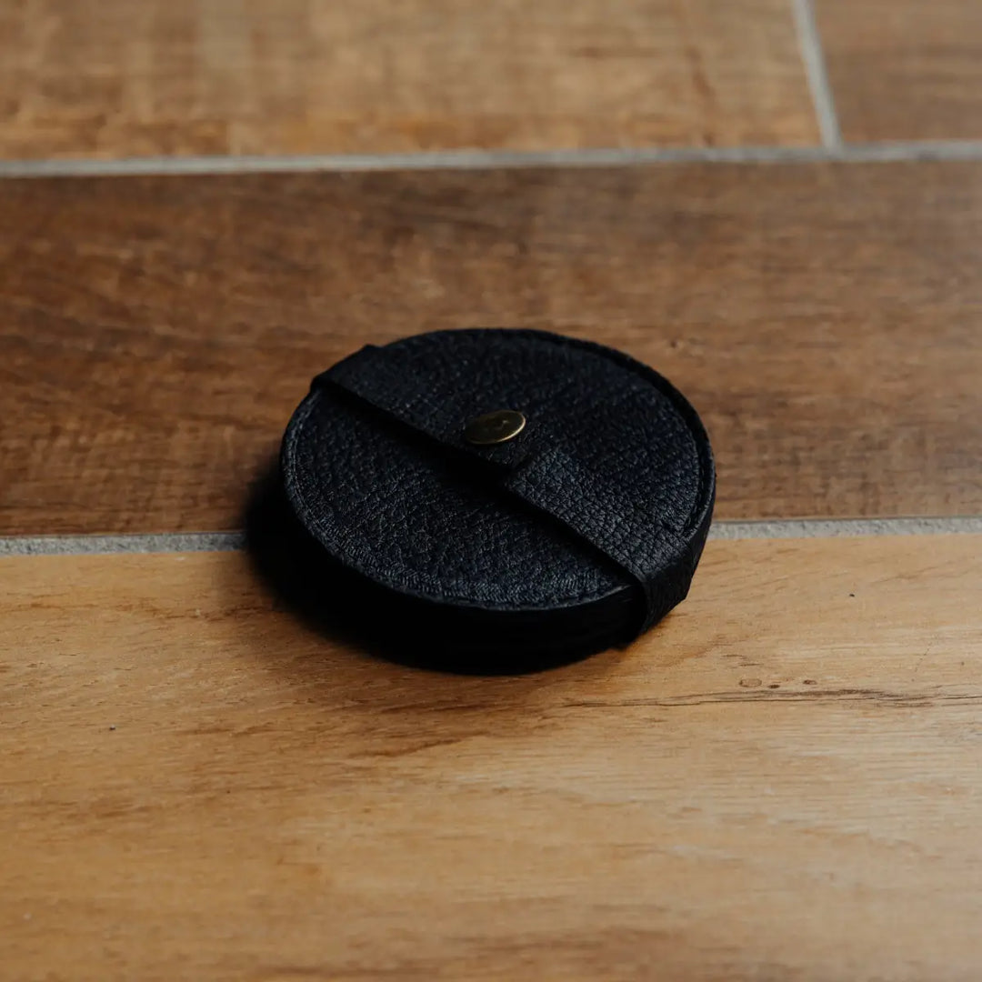 Black textured round leather coaster on a wooden surface