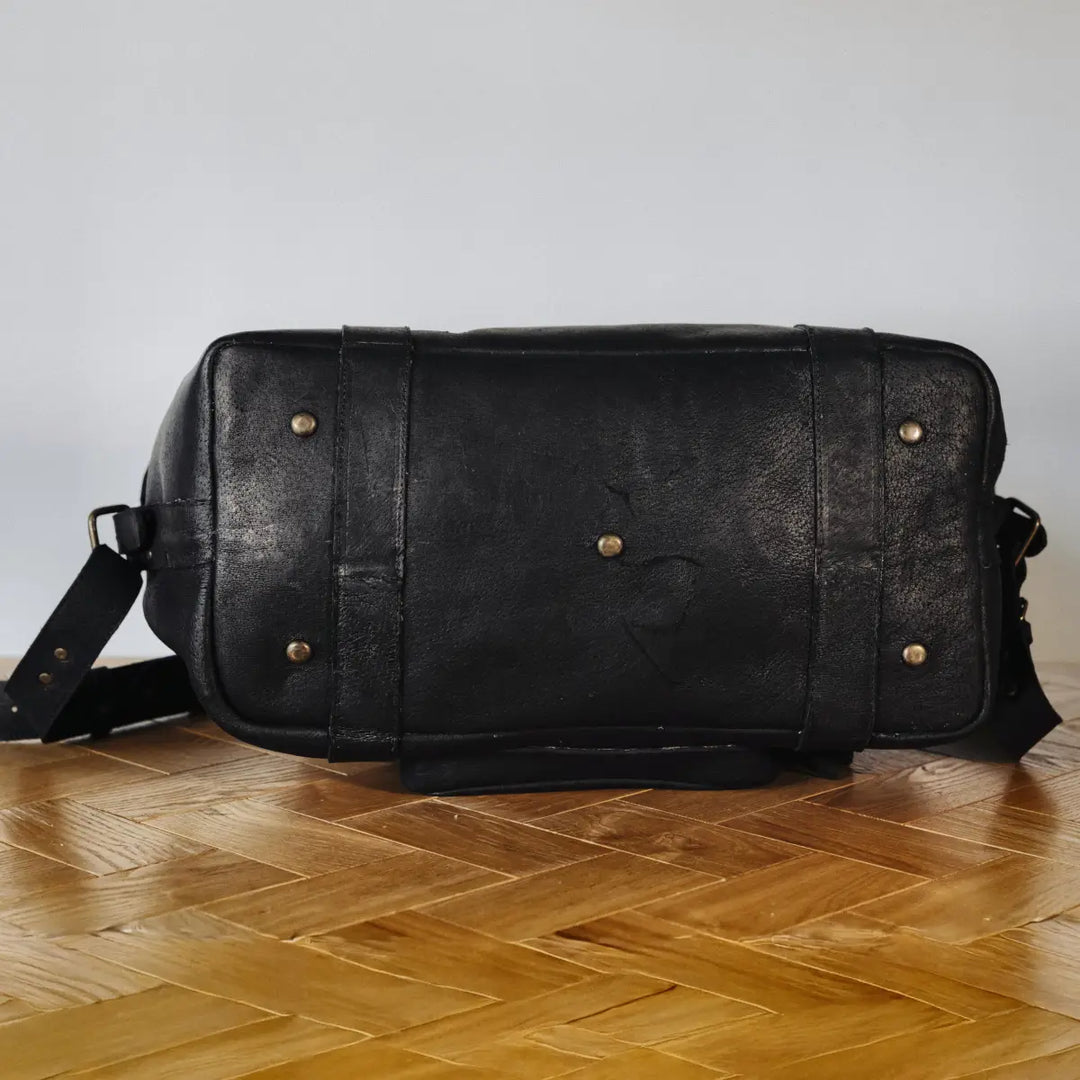 Black boar leather duffel bag with gold rivets on a wooden floor.