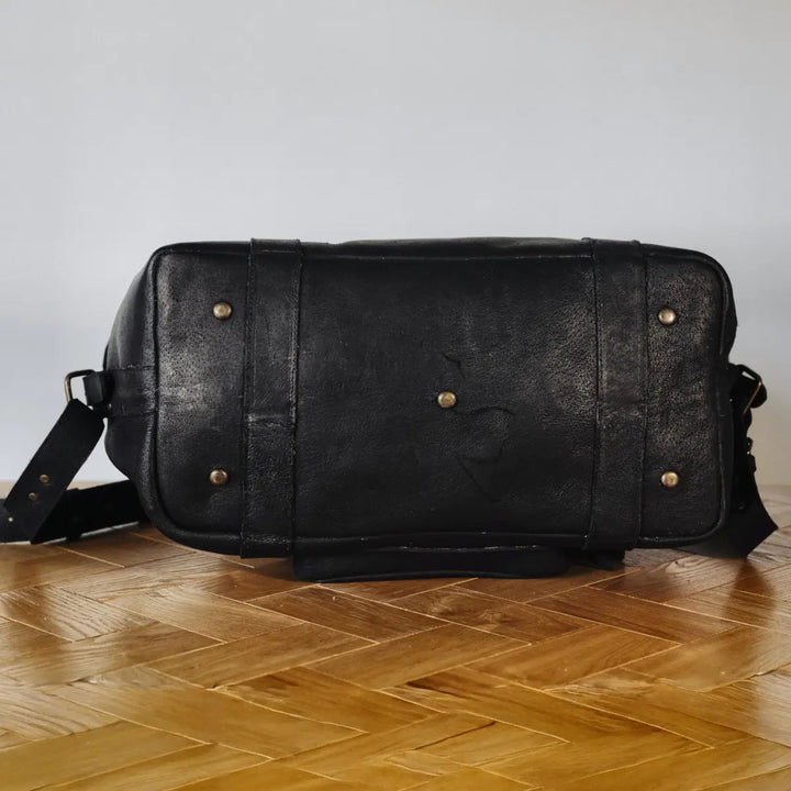Black boar leather duffel bag with gold rivets on a wooden floor.