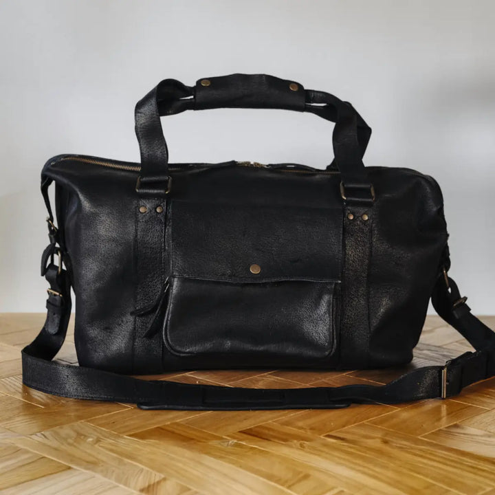 Black boar leather duffel bag on a wooden floor with a neutral background