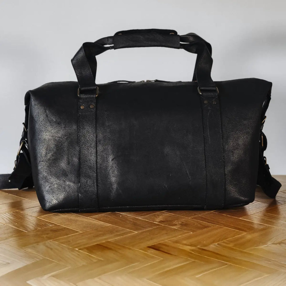 Black boar leather duffel bag on a wooden floor with a white background