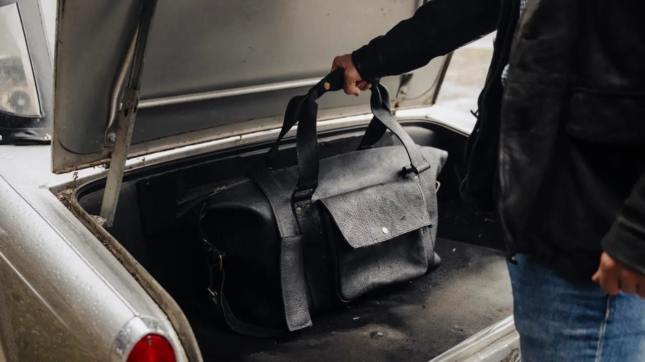Person loading a black boar leather duffel bag into the trunk of a car