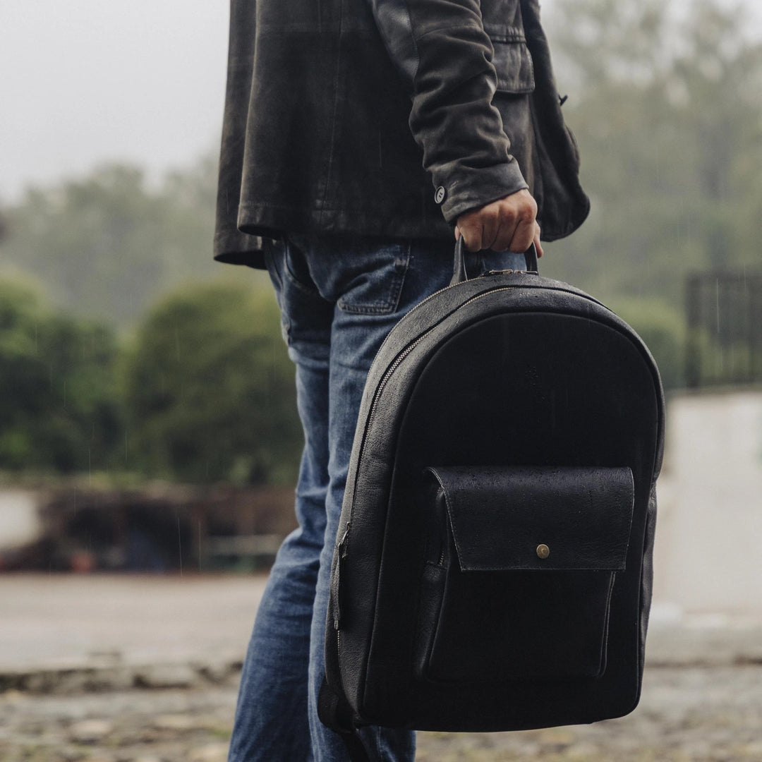 Man holding a black jabari boar leather backpack outdoors with a blurred natural background