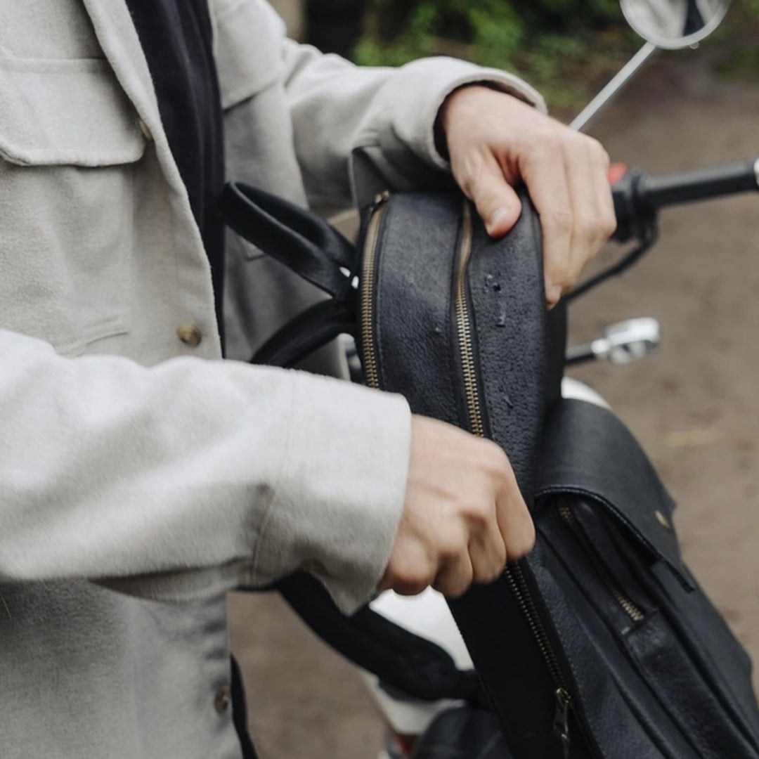 Man holding a black jabari boar leather backpack on a motorcycle with a blurred background