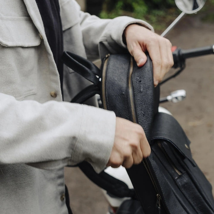 Man holding a black jabari boar leather backpack on a motorcycle with a blurred background