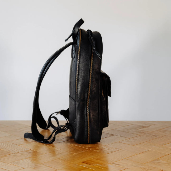 Black leather backpack on a wooden floor with a white wall background