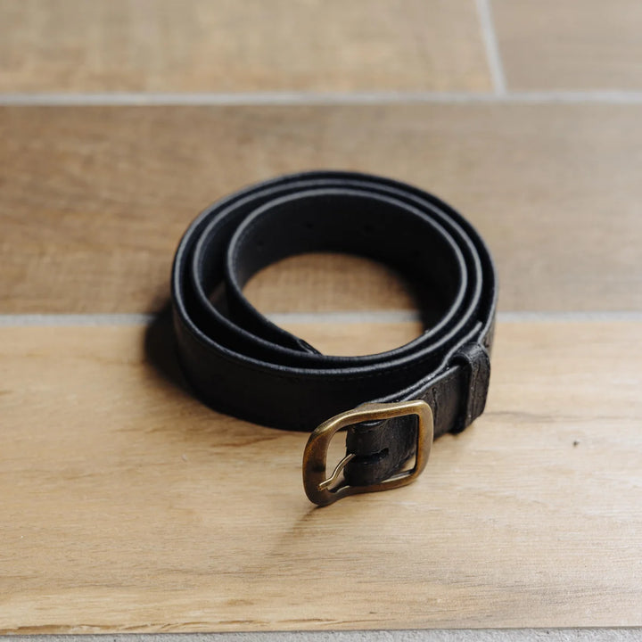 Black jabari 1.25 inch boar leather belt with a brass buckle on a wooden surface