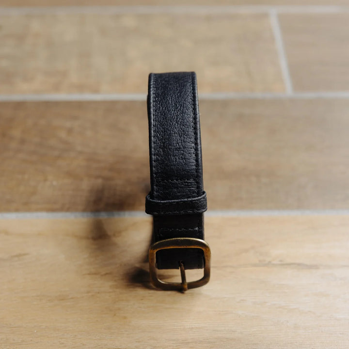 Black Jabari boar leather belt with a brass buckle on a wooden surface