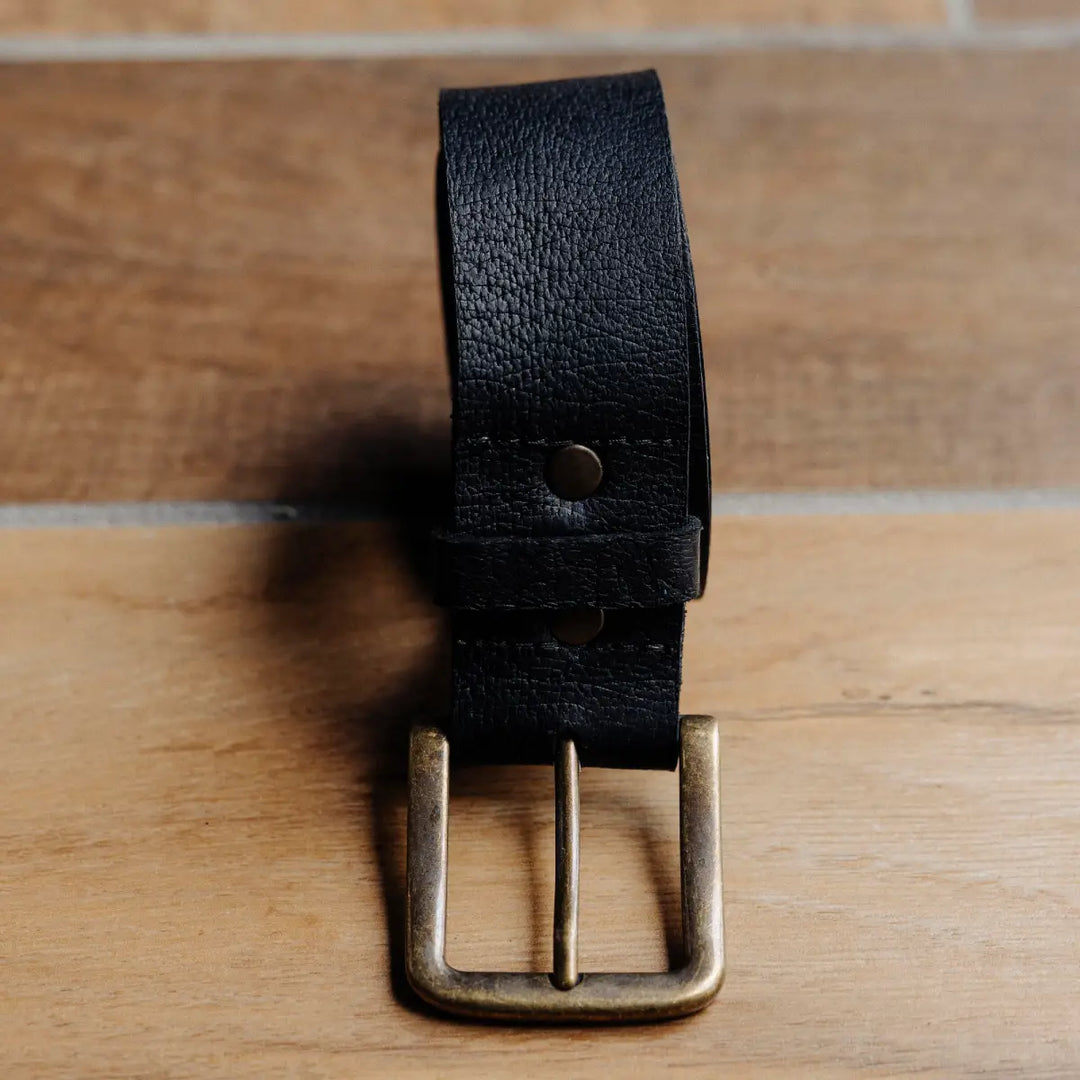 Black black jabari boar leather belt with brass buckle on a wooden surface