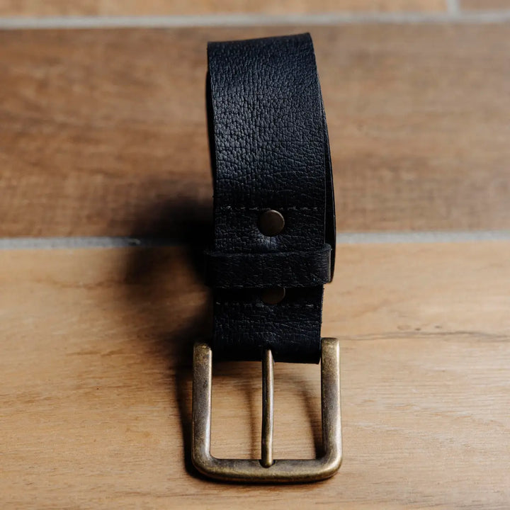Black black jabari boar leather belt with brass buckle on a wooden surface