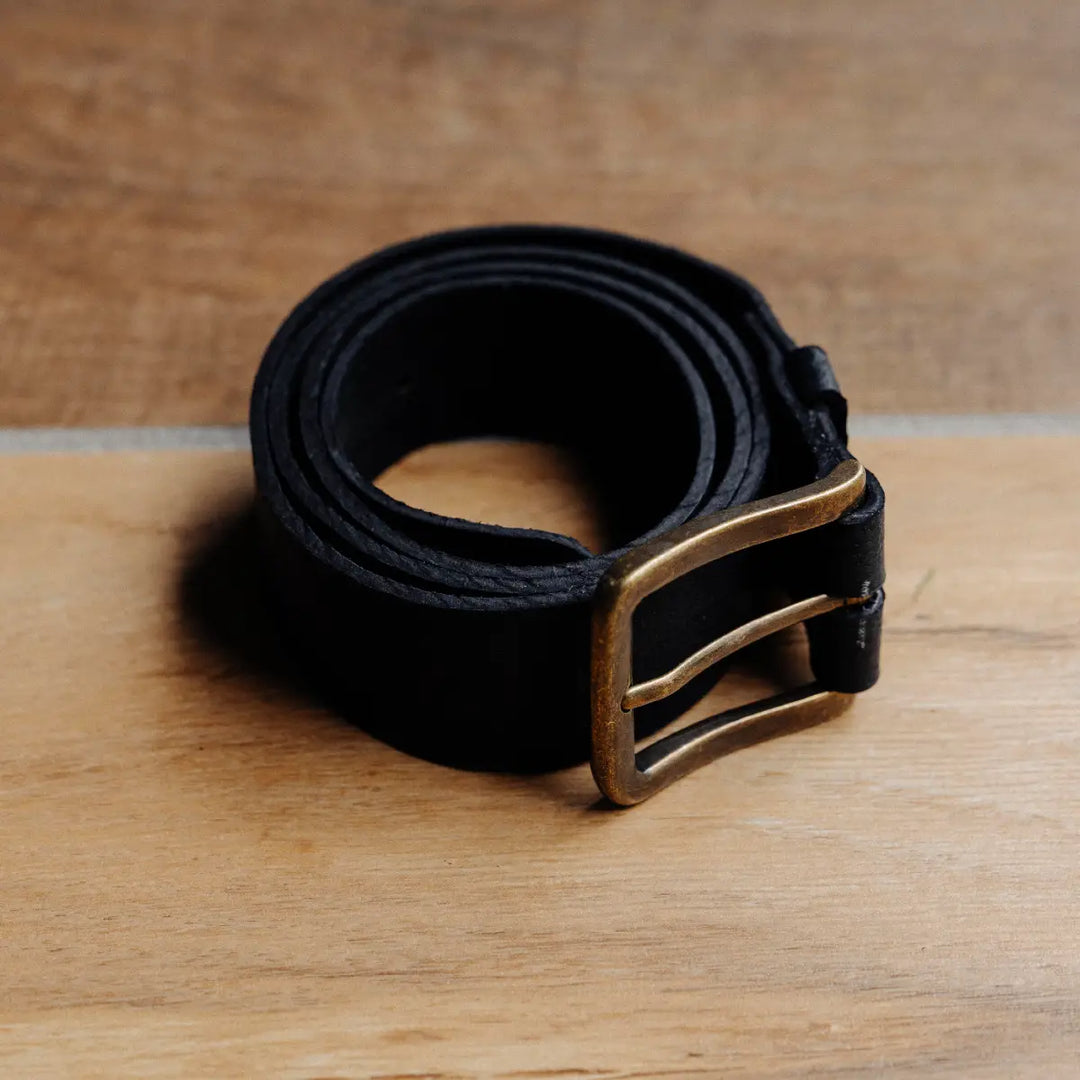 Black jabari boar leather belt with a brass buckle on a wooden surface