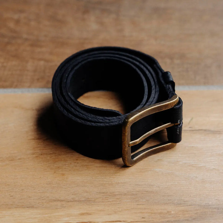 Black jabari boar leather belt with a brass buckle on a wooden surface