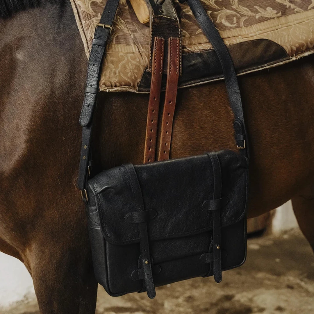 Black Jabari boar leather messenger bag attached to a horse with a patterned saddle cover.