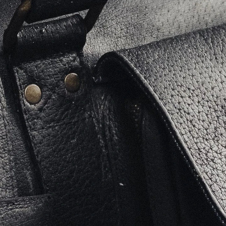 Close-up of a black boar leather duffle bag with brass rivets