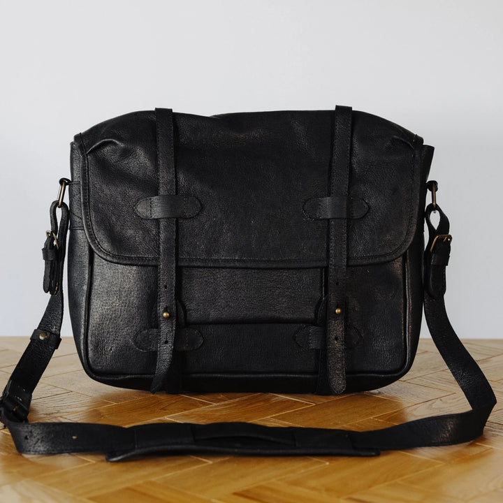 Smooth black jabari leather messenger bag on a wooden surface with a light gray background