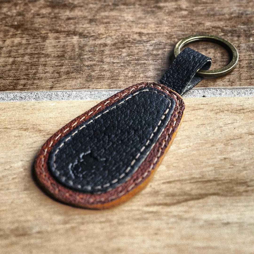 Black leather keychain with brown accents on a wooden surface
