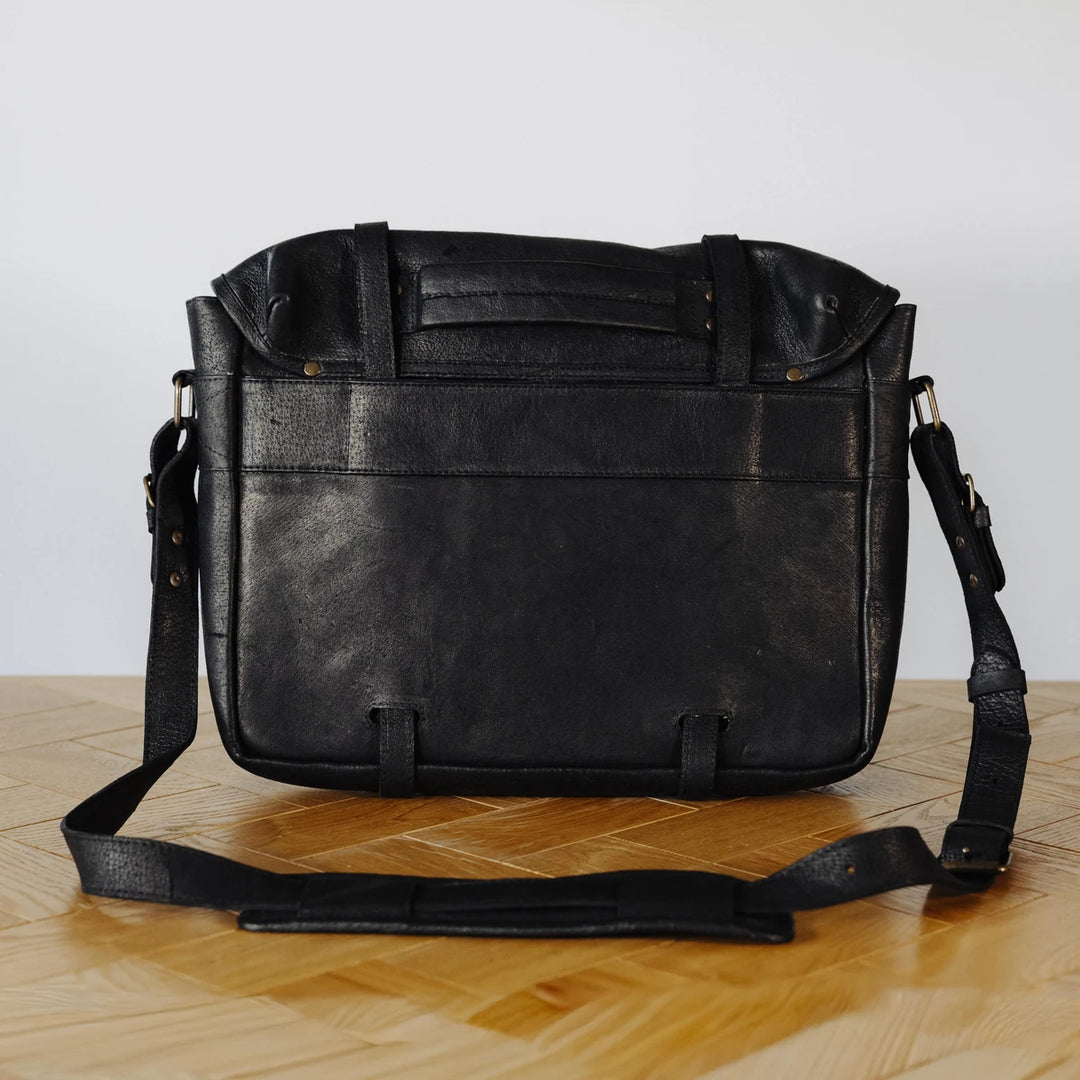 Black messenger leather bag on a wooden floor with a white background