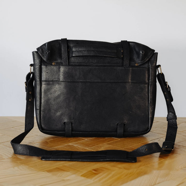 Black messenger leather bag on a wooden floor with a white background