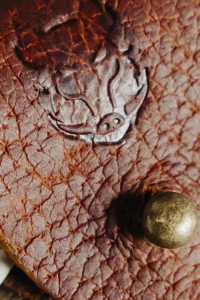 Close-up of a textured brown leather cabel wrap with a metal emblem and a gold button.