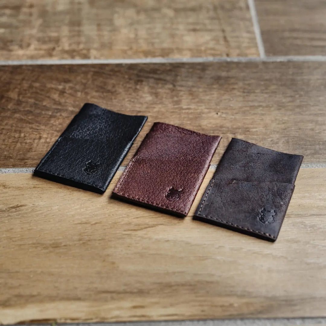 Three leather card holders in black, brown, and dark brown on a wooden surface.