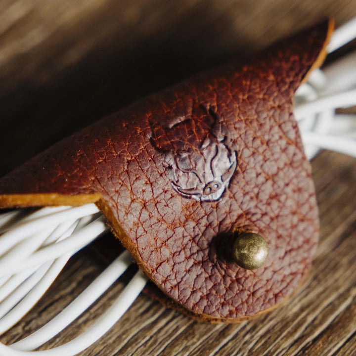 Brown cognac jabari boar leather cable wrap with a boar emblem on a wooden surface