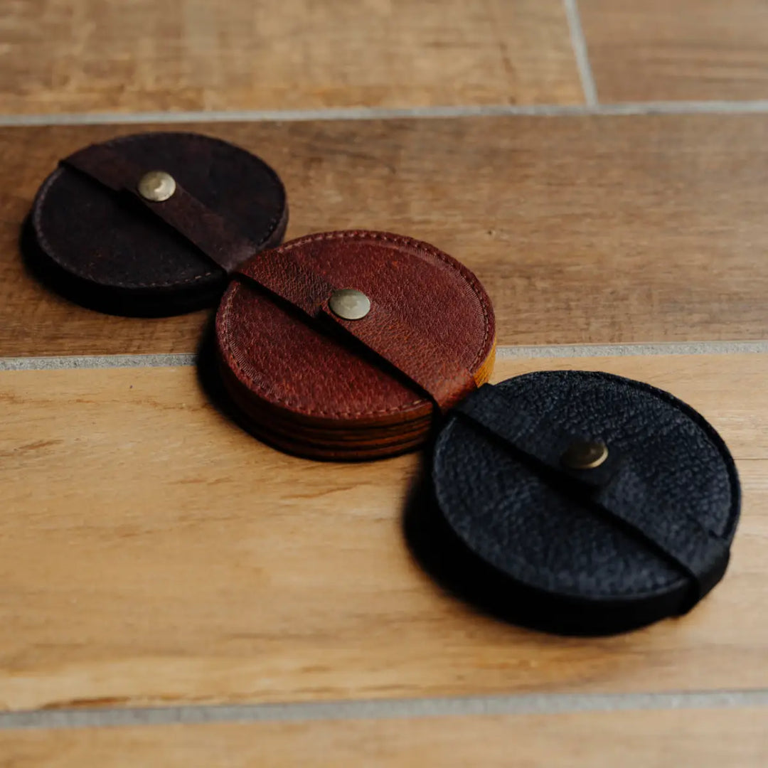 Three leather coasters in black, brown, and dark brown on a wooden surface.