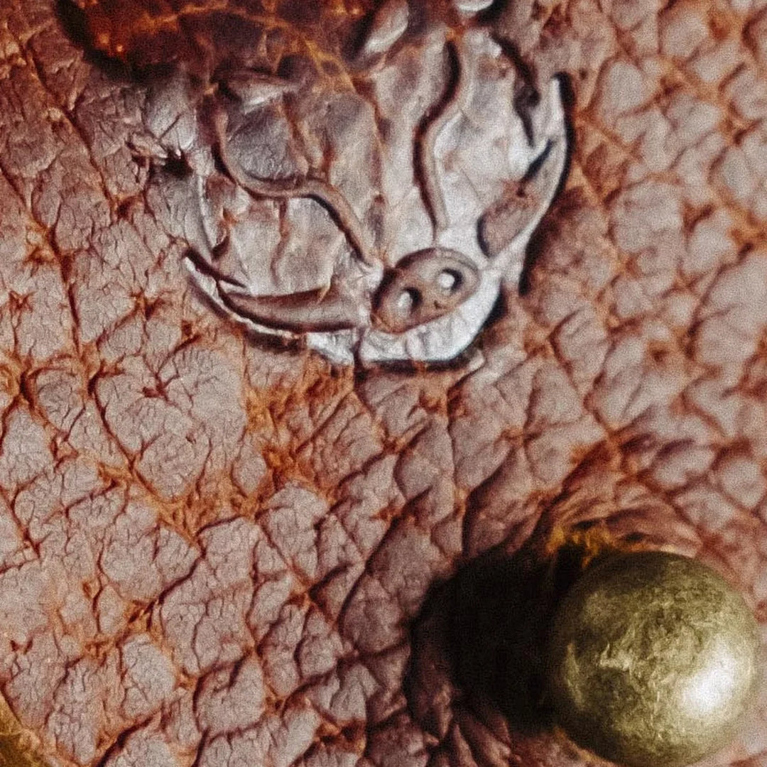 Bad leather goods logo on a distinctly grained leather surface with a brass fastener nearby