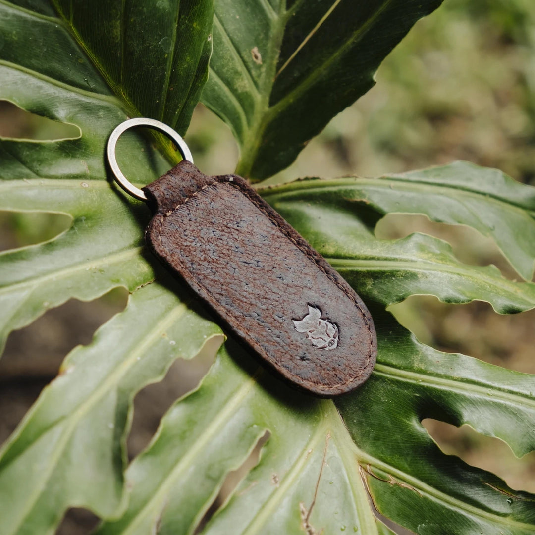 Brown boar leather keychain with a metal ring on a green leaf