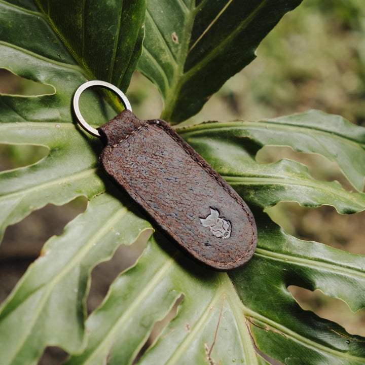 Brown boar leather keychain with a metal ring on a green leaf