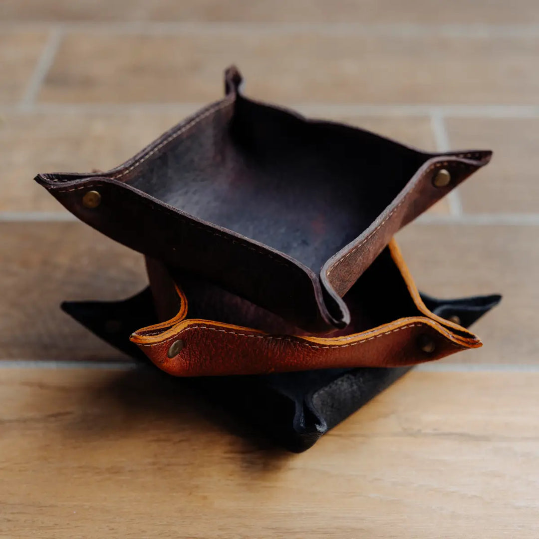 Three boar leather valet trays on a wooden surface