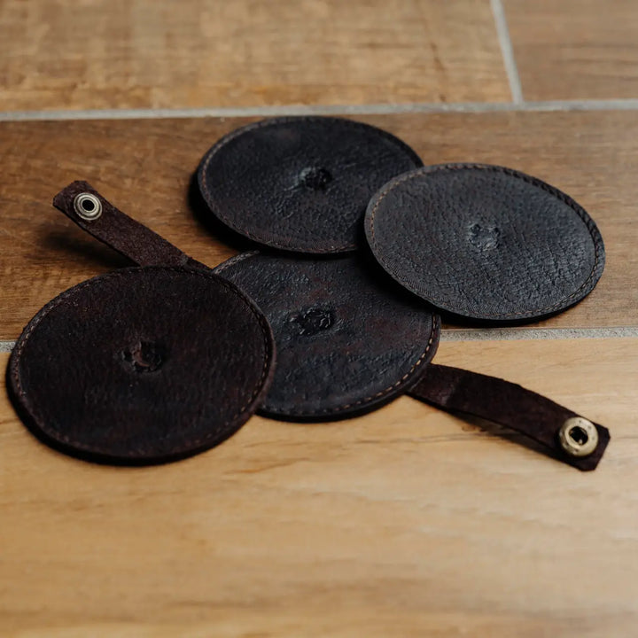 Set of black leather coasters with straps on a wooden surface