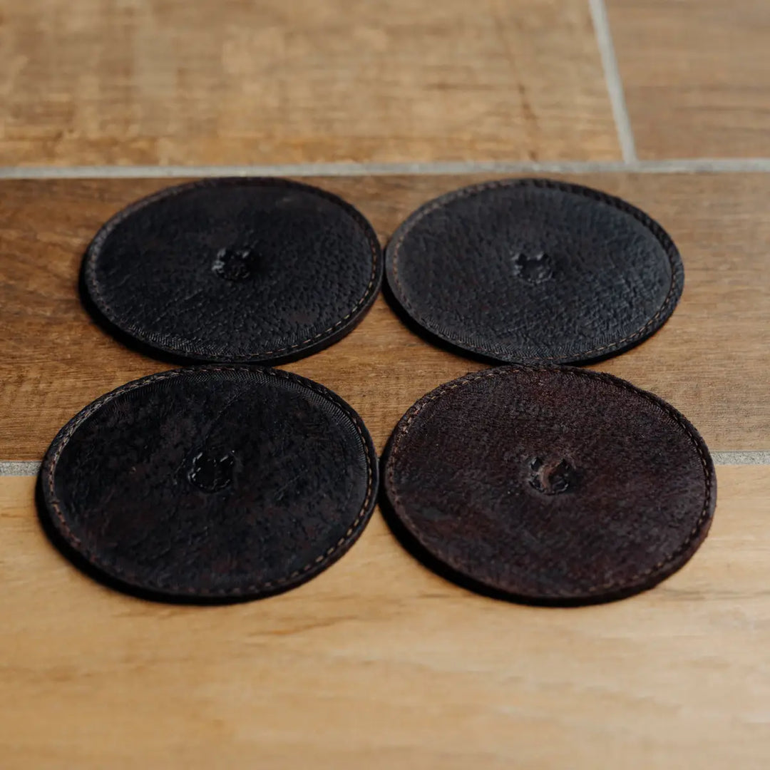 Four dark brown leather coasters on a wooden surface