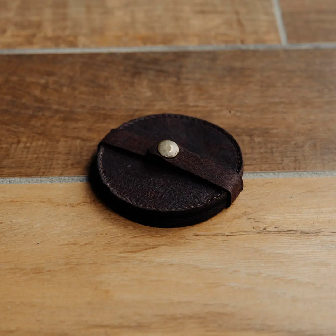 Round brown leather coaster with a metal snap on a wooden surface