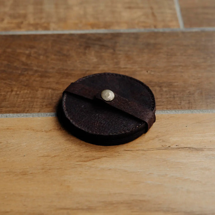 Round brown leather coaster with a metal snap on a wooden surface
