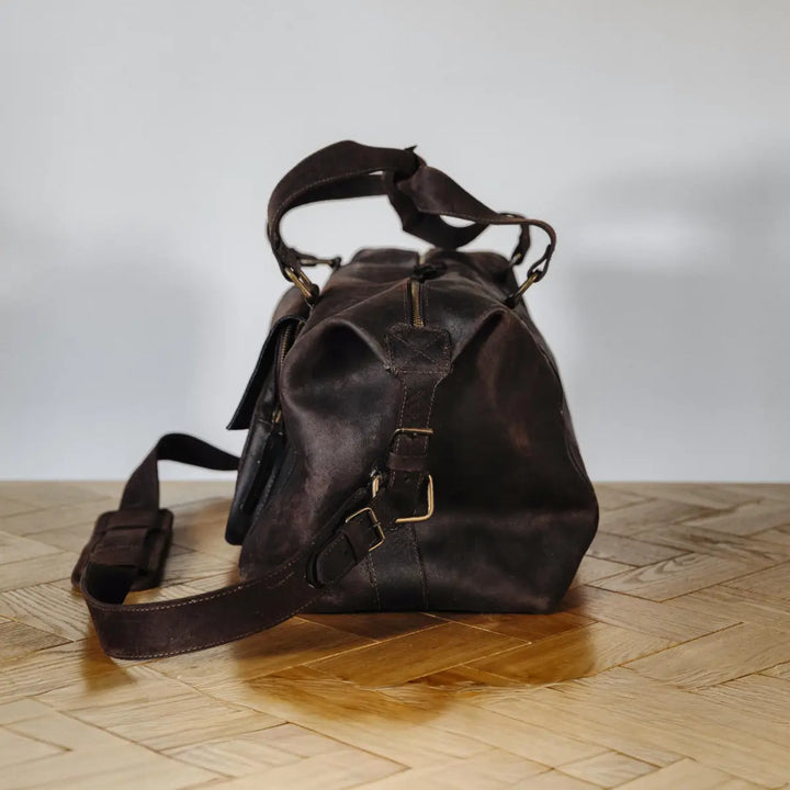 Dark brown waxy chocolate boar leather bag on a wooden floor with a white background