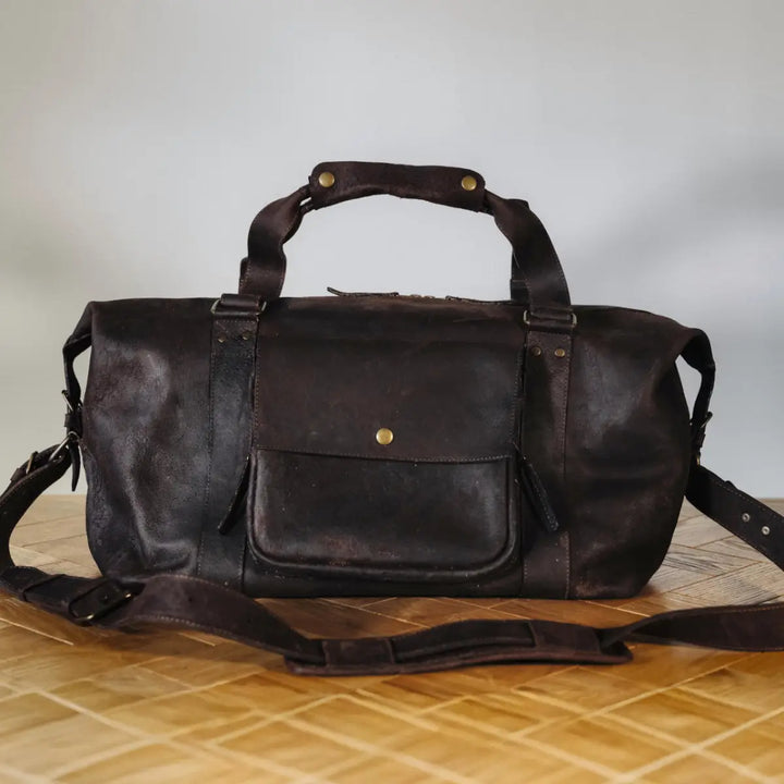 dark brown boar leather duffel bag on a wooden surface with a neutral background