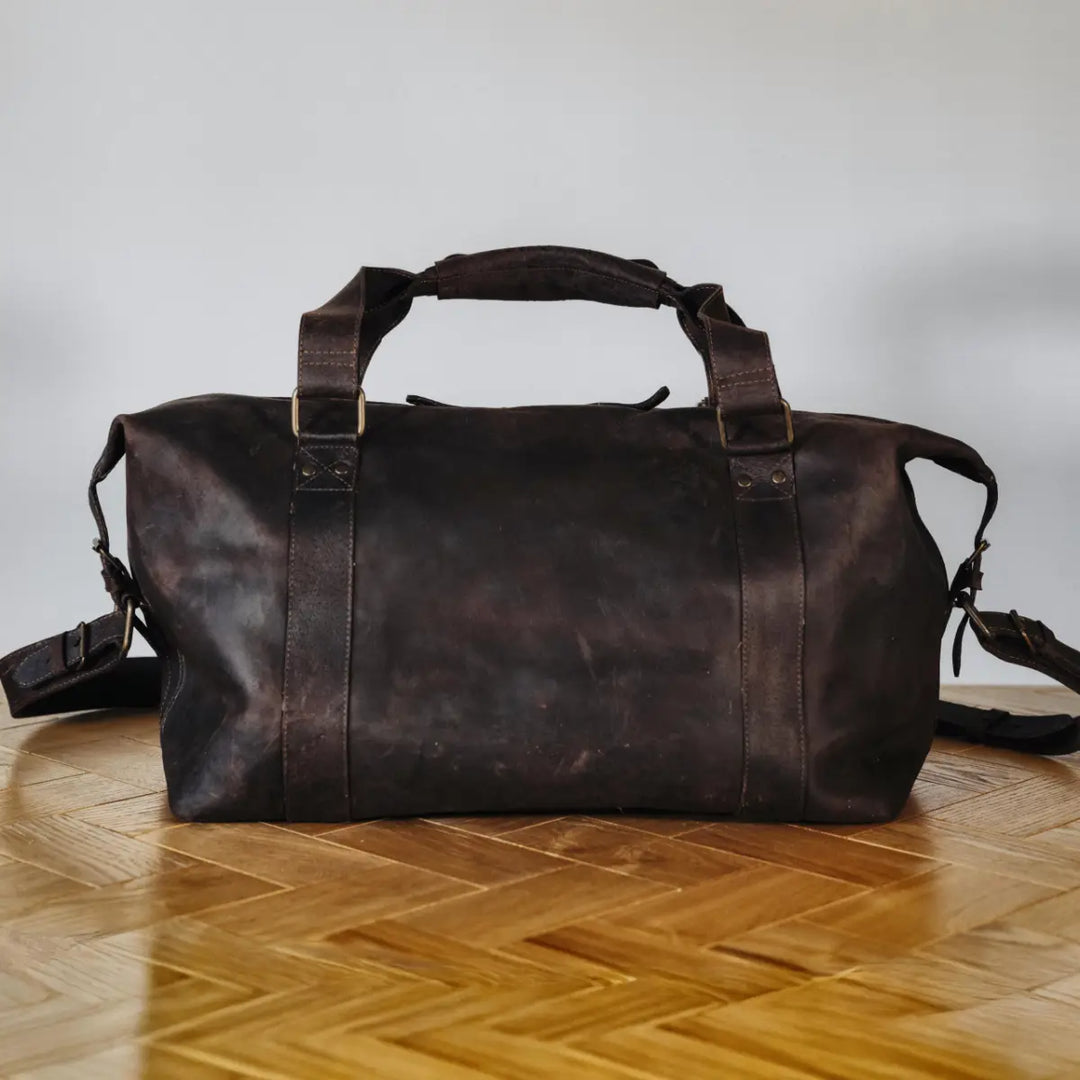 Dark brown boar leather duffel bag on a wooden floor with a neutral background