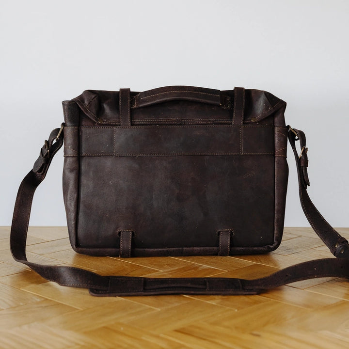Brown leather messenger bag on a wooden surface with a light gray background