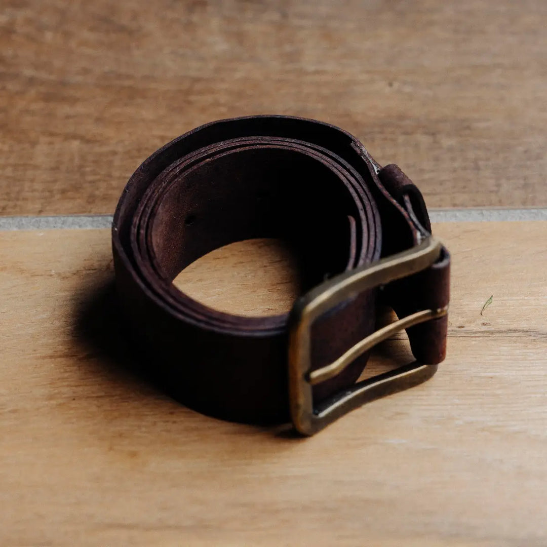 Brown chocolate waxy boar leather belt with a brass buckle on a wooden surface
