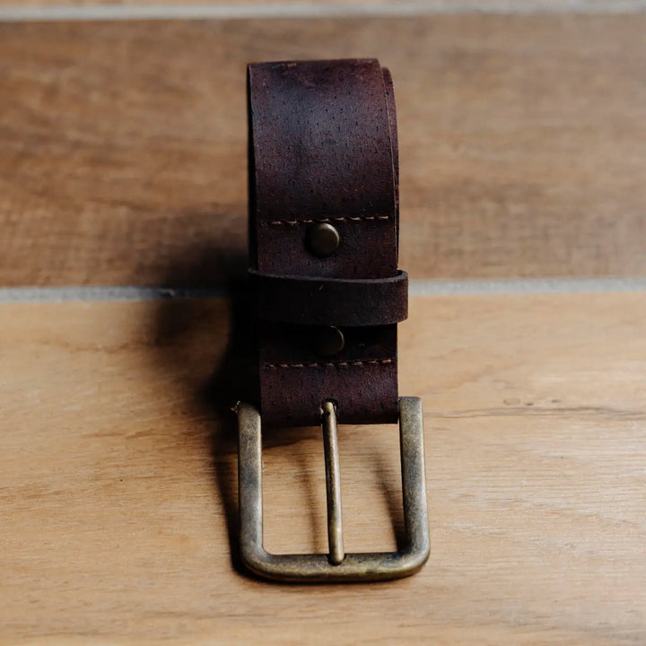 Brown chocolate waxy boar leather belt with brass buckle on a wooden surface