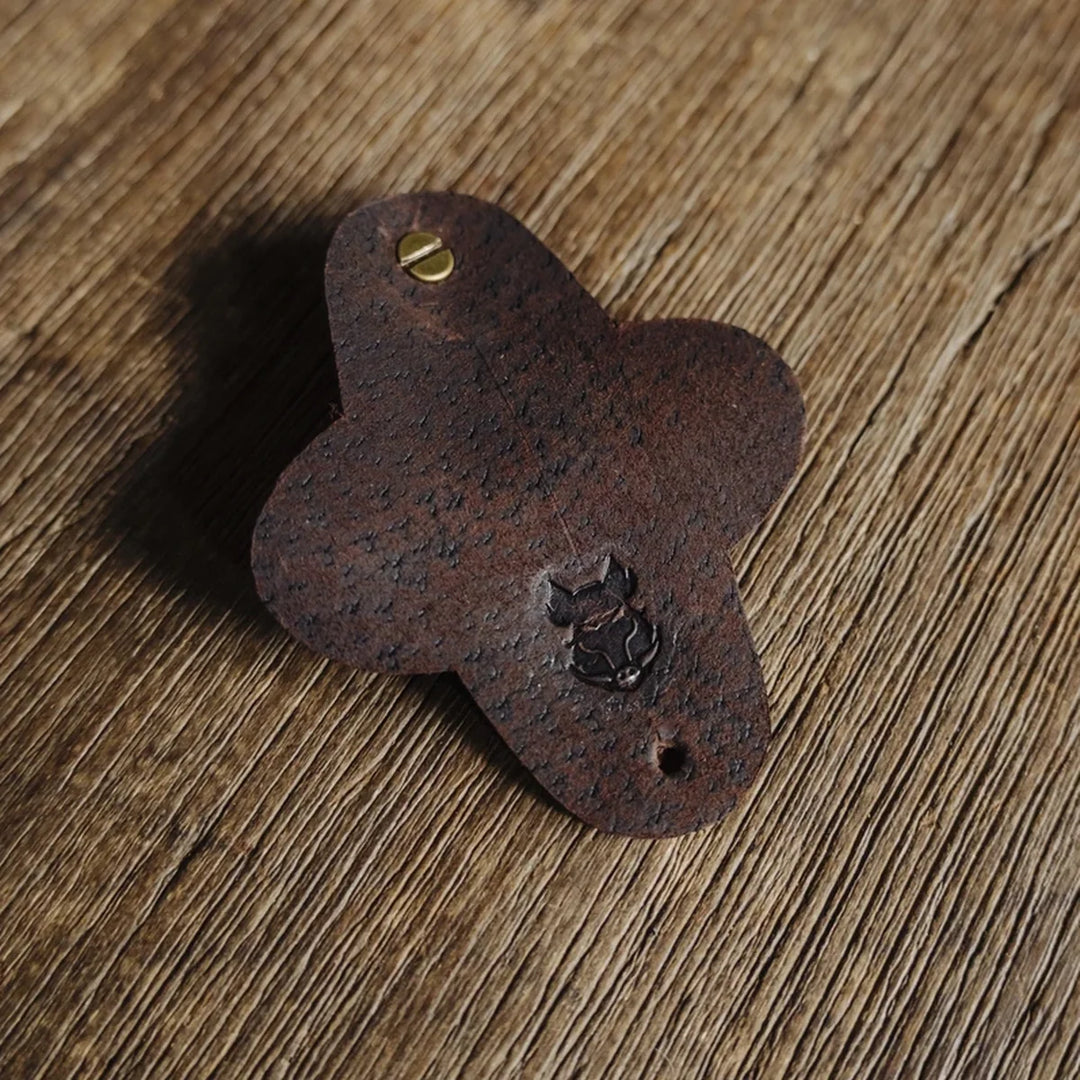 Dark brown chocolate waxy boar leather cable wrap with a small Bad Leather's Goods boar emblem on a wooden surface.