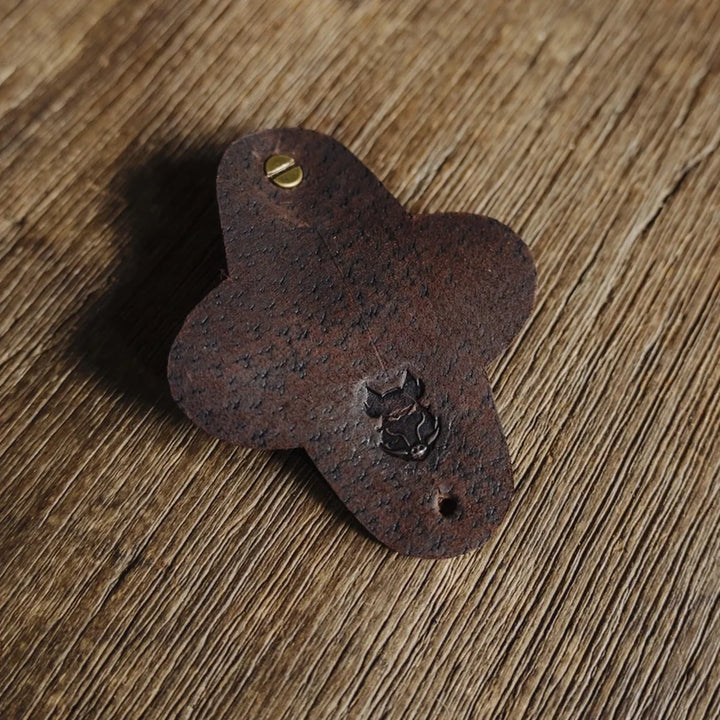 Dark brown chocolate waxy boar leather cable wrap with a small Bad Leather's Goods boar emblem on a wooden surface.